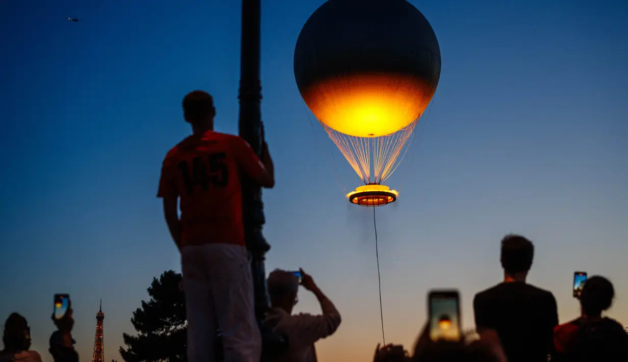 Orang-orang menyaksikan kaldron Olimpiade Paris 2024 saat matahari terbenam di Jardin des Tuileries di Paris pada 28 Juli 2024. (Dimitar DILKOFF/AFP)