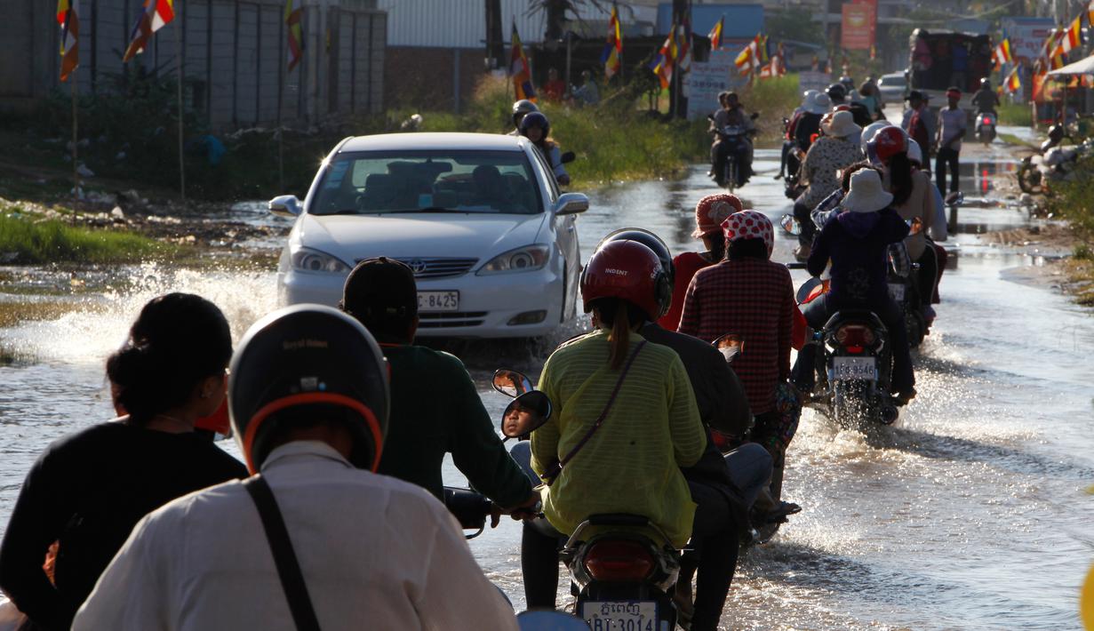 Penduduk desa mengendarai sepeda motor mereka di jalan banjir di desa Trapang Anchanh, di luar Phnom Penh, Kamboja, (27/10). (AP Photo/Heng Sinith)