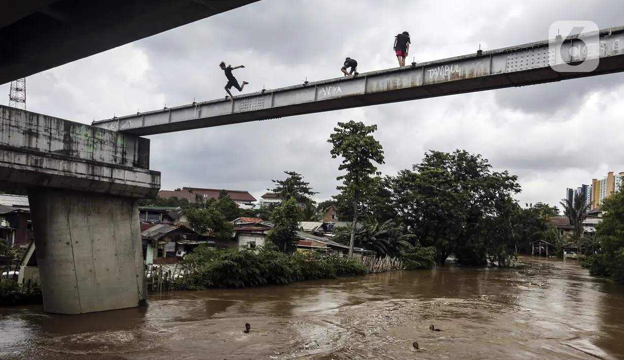 Anak-anak melompat ke Sungai Ciliwung saat banjir melanda Jalan Bina Warga Rt 005/Rw 07 Kelurahan Rawa Jati, Jakarta, Senin (8/2/2021). Banjir setinggi 60-190 cm tersebut disebabkan oleh luapan air Sungai Ciliwung dan curah hujan Jakarta yang tinggi. (Liputan6.com/Johan Tallo)