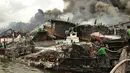 Pekerja dan petugas pemadam kebakaran mencoba memadamkan api di kapal nelayan di Pelabuhan Benoa, Denpasar, Bali, Senin (9/7). Kebakaran besar melalap 39 kapal yang tengah bersandar di dermaga. (SONNY TUMBELAKA/AFP)