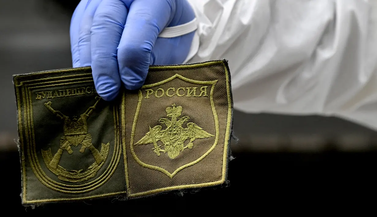 Seorang ahli forensik Ukraina menunjukkan tambalan yang ditemukan pada tubuh seorang tentara Rusia yang digali di Desa Zavalivka, sebelah barat Kiev, Ukraina, 11 Mei 2022. Hingga saat ini, lebih dari 230 jenazah tentara Rusia telah dikumpulkan dan disimpan di Ukraina dengan sebagian besar ditemukan di pinggiran ibu kota. (Sergei SUPINSKY/AFP)