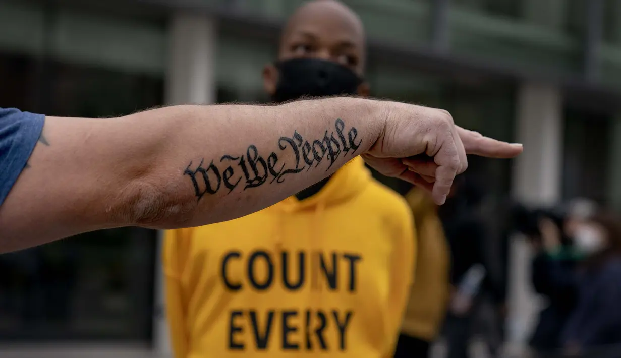 Tato "We The People" menghiasi lengan pendukung Donald Trump, Bob Lewis (kiri) saat dia berdebat dengan kontra pemrotes Ralph Gaines sementara pendukung Trump berdemonstrasi menentang hasil pemilu di luar papan penghitungan pusat di tcf Center, Detroit, Kamis (5/11/2020). (AP Photo/David Goldman)