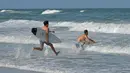 Peselancar berlari ke ombak ketika pantai dibuka di Jacksonville Beach, Florida (17/4/2020). Pengumuman DeSantis pada hari Jumat datang ketika pantai Florida utara menjadi yang pertama yang memungkinkan pengunjung pantai untuk kembali sejak penutupan.  (Will Dickey/The Florida Times-Union via AP)