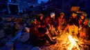 Tim penyelamat duduk di dekat api unggun di Hatay, Turki, Minggu (12/2/2023). Cuaca dingin menjadi tantangan bagi tim penyelamat untuk menemukan para penyintas yang terjebak di bawah reruntuhan bangunan. (Yasin AKGUL/AFP)
