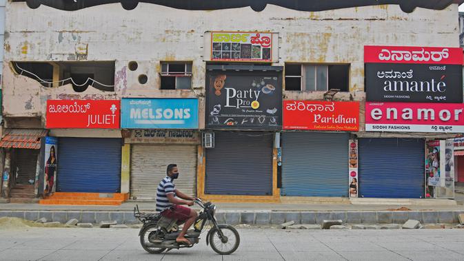 Pengendara motor melintas di depan pertokoan yang tutup di area komersial saat lockdown di Bangalore, Rabu (15/7/2020). Pusat IT India, Bangalore, kembali memberlakukan lockdown selama seminggu dimulai dari 14 Juli 2020 untuk menahan lonjakan kasus Covid-19 yang meningkat. (Manjunath Kiran/AFP)