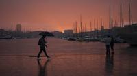 Seorang pria berjalan dengan payung saat pasangan melihat langit di Pelabuhan Vieux Marseille saat badai di Marseille, Prancis selatan, Senin (4/10/2021). Wilayah Prancis selatan dalam siaga untuk hujan lebat dan banjir. (AP Photo/Daniel Cole)