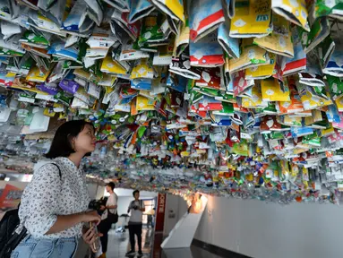 Seorang wanita melihat instalasi seni gantung sekelompok seniman yang terbuat dari sisa-sisa plastik, kaleng dan wadah di sebuah pameran "Reduce the Litter" di Pusat Kebudayaan Prancis di Hanoi (15/7/2019). Pameran ini mengambil perspektif tentang produksi dan konsumsi. (AFP Photo/Nhac Nguyen)