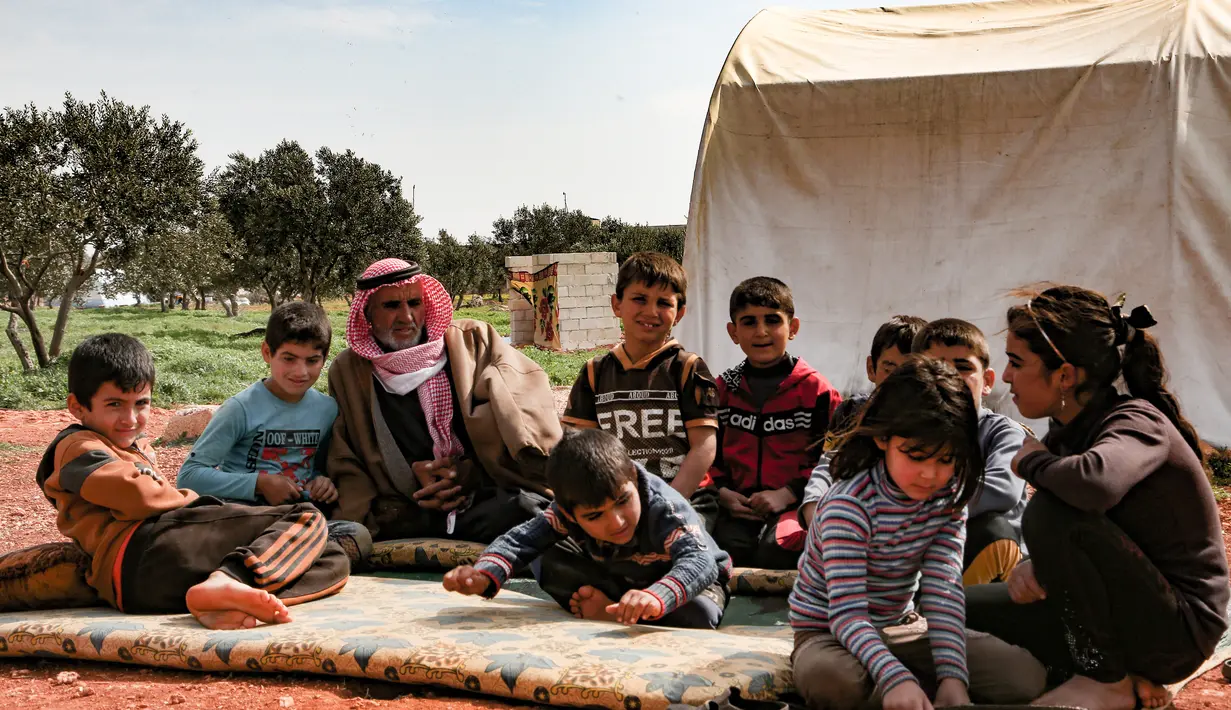 Abderrazaq Khatoun, beristirahat dengan 11 cucunya yang yatim piatu di luar tenda di desa Harbanoush, di Idlib, Suriah pada 11 Maret 2021. Perang Suriah yang merampas 13 anak Khatoun dan salah satu istrinya, membuat kakek 83 tahun itu membesarkan 11 cucu yatim piatu sendirian. (Ahmad al-ATRASH/AFP)