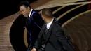 Will Smith (kanan) memukul presenter Chris Rock di atas panggung Piala Oscar 2022 saat penghargaan untuk film dokumenter terbaik di Dolby Theatre, Minggu (27/3/2022). Will Smith merasa lawakan sang komedian terkait istrinya, Jada Pinkett Smith keterlaluan. (Neilson Barnard/Getty Images/AFP)