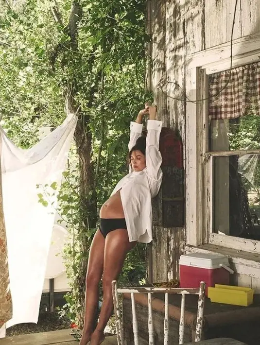 Gaya kasual Hailey Bieber di sebuah pemotretan. Terlihat ia mengangkat kedua tangannya ke atas, mengenakan atasan kemeja lengan panjang putih dipadu dengan celana dalam hitam, memperlihatkan kulitnya yang eksotis. [Foto: Instagram/jdblegend_]