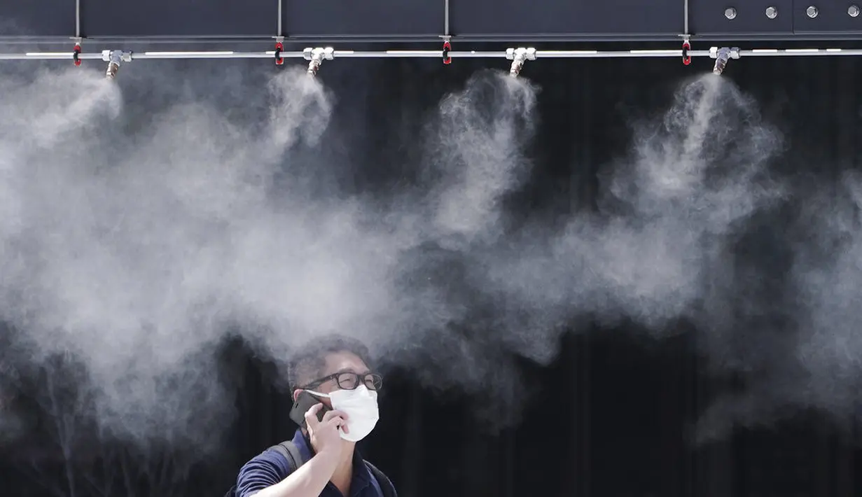 Seorang pria mengenakan masker untuk mencegah penyebaran Covid-19 di bawah titik kabut dingin di Tokyo (12/8/2020). Menurut Badan Meteorologi Jepang, cuaca panas telah ditetapkan dengan suhu naik lebih dari 34 derajat Celcius (93,2 derajat Fahrenheit) di Tokyo. (AP Photo/Eugene Hoshiko)