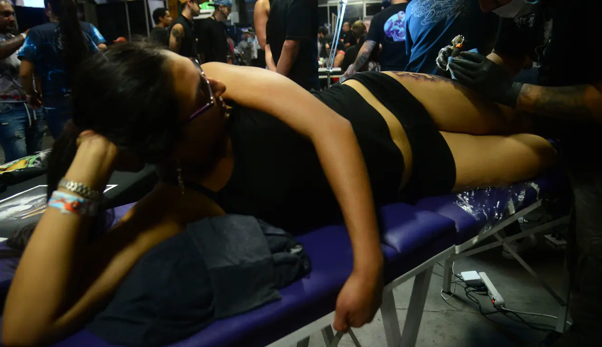 Seorang wanita terbaring saat membuat tato dikakinya di Expotattoo Colombia 2016 di Medellin, (16/7). Para wanita penggila tato di Kolombia tidak mensia-siakan pameran tato tersebut untuk memperbanyak tato di tubuhnya. (AFP PHOTO/RAUL Arboleda)
