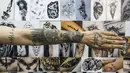 Klien Naim Abdallah memamerkan tato baru di lengan dan tangannya di samping dinding yang menampilkan ilustrasi karya dan desain tatto Naim Abdallah di ruang tamu di Kota Betlehem di Tepi Barat (24/1/2021). (AFP/Hazem Bader)