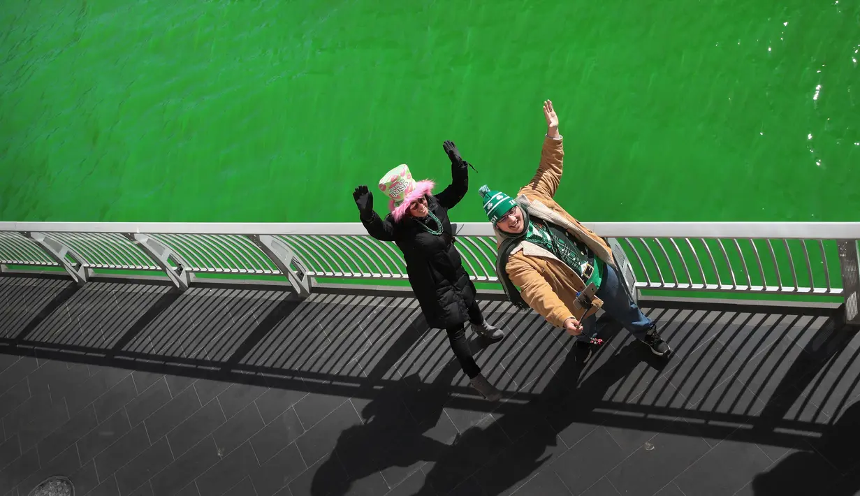 Wisatawan berfoto dengan latar belakang sungai Chicago, AS yang berwarna hijau, 11 Maret 2017. Hijaunya warna sungai tersebut sebenarnya berasal dari cairan pewarna khusus untuk perayaan St. Patrick's Day (SCOTT OLSON/GETTY IMAGES NORTH AMERICA/AFP)