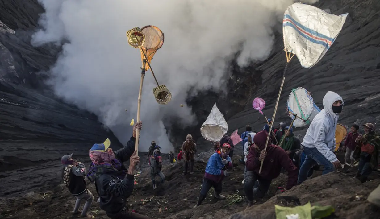 Orang-orang mencoba menangkap sesajen yang dilemparkan suku Tengger ke kawah Gunung Bromo saat upacara Yadnya Kasada di Probolinggo, Jawa Timur, Sabtu (26/6/2021). Suku Tengger mempersembahkan sesajen berupa beras, buah, ternak, dan barang lainnya untuk mencari berkah dari dewa. (Juni Kriswanto/AFP)