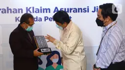 Direktur AXA Mandiri Uke Giri Utama (tengah) memberikan cinderamata kepada Ketua Umum DPP Persatuan Perawat Nasional Indonesia (PPNI) dr. Harif Fadillah (kiri) menyerahkan klaim tahap pertama kepada 170 tenaga kesehatan yang gugur menangani COVID-19 di Jakarta (26/8/2021). (Liputan6.com/HO/Alwi)