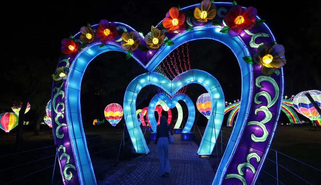 Seorang wanita berjalan melewati instalasi lampu di Dubai Garden Glow, Dubai, Uni Emirat Arab, 1 November 2021. Instalasi tersebut dibuat dari lebih satu juta bohlam penghemat energi dan kain bercahaya daur ulang karya seniman seluruh dunia. (GIUSEPPE CACACE/AFP)