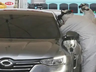 Petugas medis dengan pakaian pelindung mengambil sampel dari pengemudi di layanan "drive-thru" di Goyang,  1 Maret 2020. Untuk mengefisiensi waktu, pemerintah Korea Selatan membuat layanan tes uji virus corona COVID-19 kepada warganya via drive thru (tanpa turun). (AP/Ahn Young-joon)