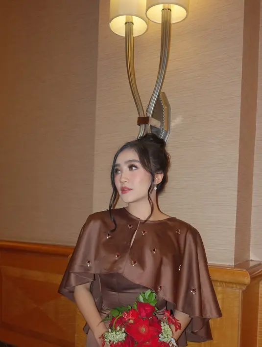 Dipadu dengan outer cape berpayet sembari membawa rangkaian bunga merah [@febbyrastanty]
