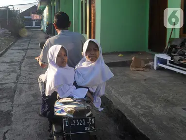 Kembar siam Al Dewi Putri Ningsih (9) dan Al Putri Anugrah (9) dibonceng sang ayah Iwan Kurniawan (43) menuju sekolah mereka di kawasan Sucinaraja, Garut, Jawa Barat, Senin (22/5/2023). (merdeka.com/Arie Basuki)