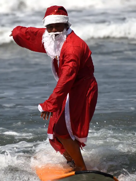 Seorang pria berkostum Santa Claus berselancar di Pantai Kuta, Bali, Senin (10/12). Setiap tahunnya, ribuan wisatawan mendatangi Bali saat menjelang natal dan tahun baru. (AFP PHOTO / Sonny Tumbelaka)