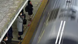 Penumpang mengenakan masker untuk mencegah penyebaran virus corona menunggu kereta di stasiun di Tokyo (8/2/2021).  Jumlah infeksi virus corona di Ibu Kota Tokyo, Jepang, meningkat sampai sembilan kali lipat sejak akhir musim panas lalu. (AP Photo/Eugene Hoshiko)