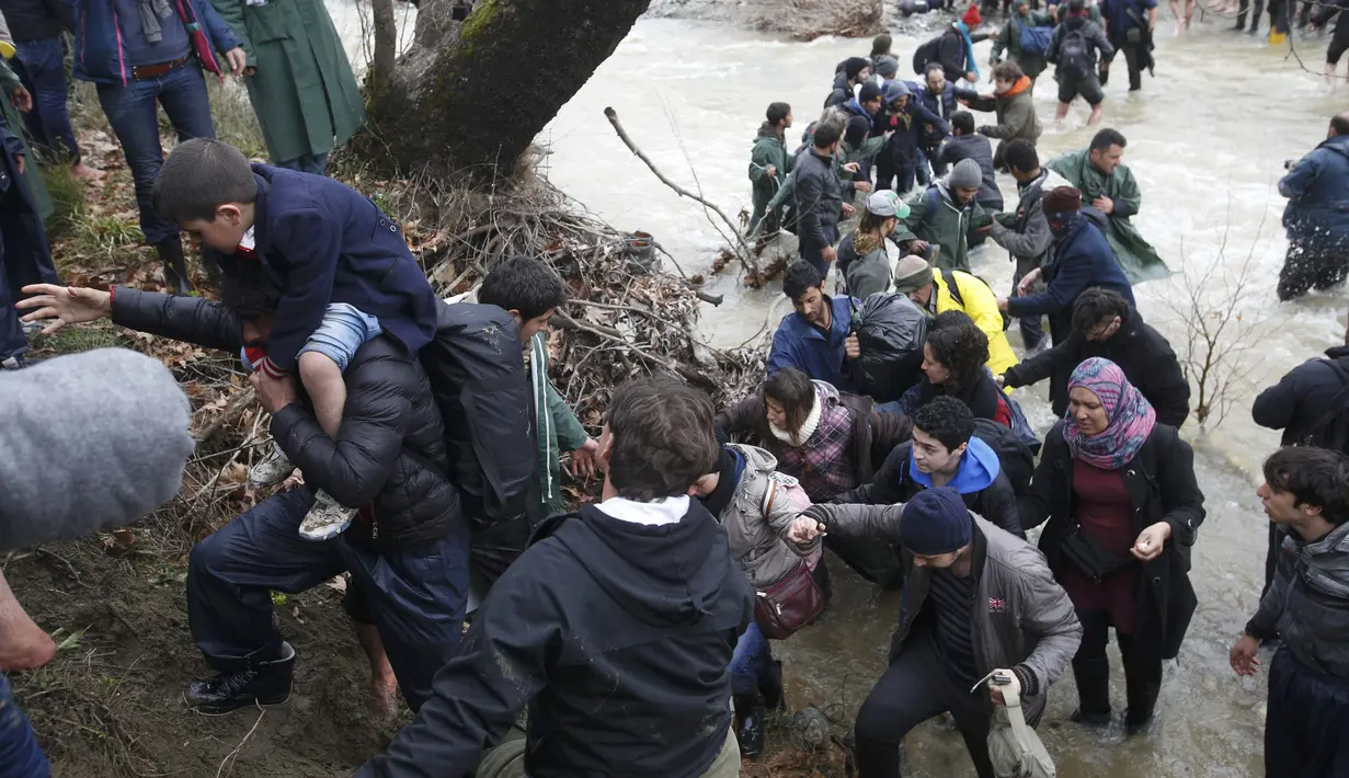 Ribuan migran menyeberangi sungai dengan berpegangan pada seutas tali di perbatasan Yunani-Makedonia, Idomeni, Yunani (14/3/2016). Lebih dari 1.000 migran nekat menembus sungai untuk mencari jalan keluar perbatasan. (Reuters/Stoyan Nenov)