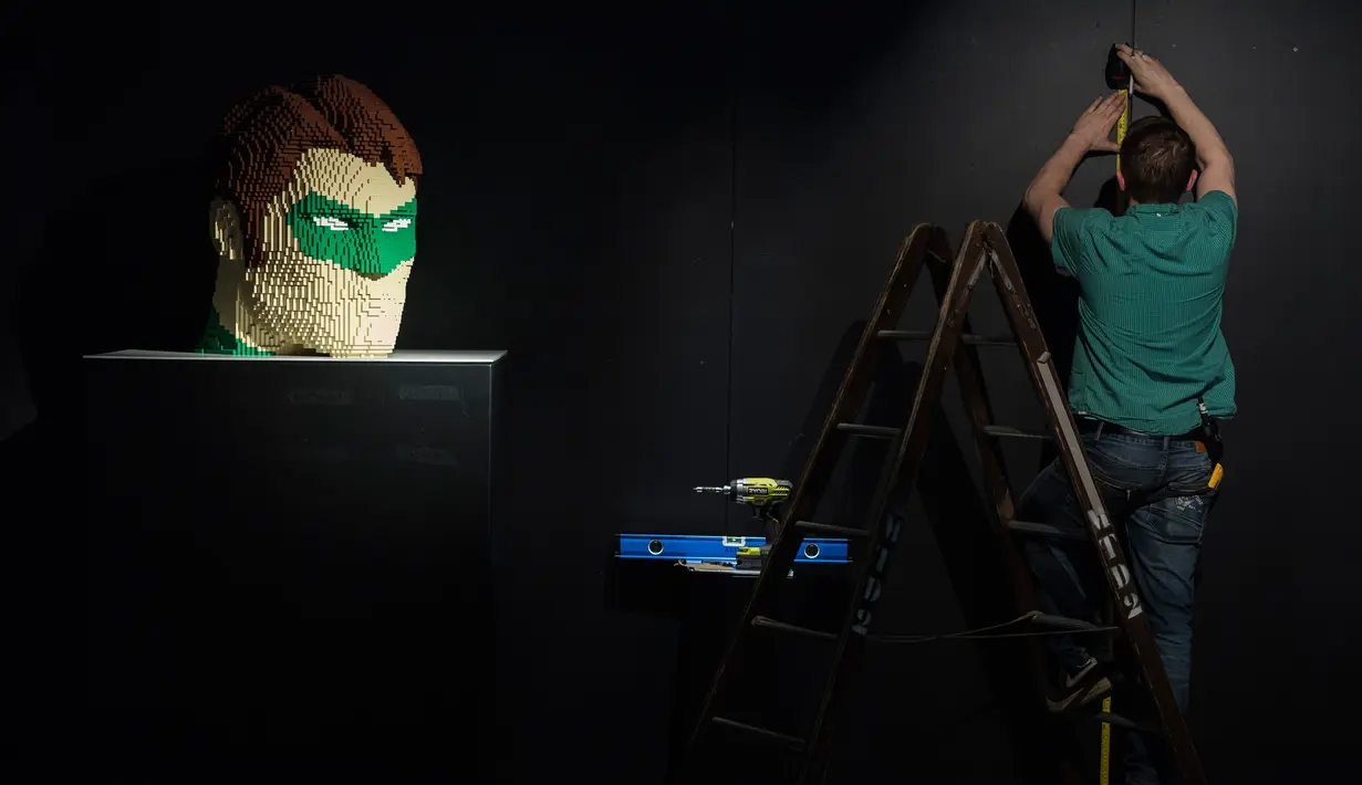 Seorang pria bekerja dekat kepala salah satu karakter pahlawan superhero DC yang dibuat dari Lego pada pameran Art of the Brick di La Vilette, Paris, Kamis (26/4). Pameran ini berlangsung hingga 19 Agustus 2018. (AFP/Lionel BONAVENTURE)