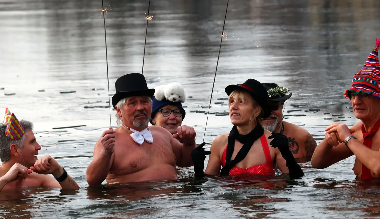 Sejumlah anggota klub renang es "Berliner Seehunde" berendam sambil bermain kembang api di danau Orankesee, Berlin, Jerman (1/1). (REUTERS/Fabrizio Bensch)