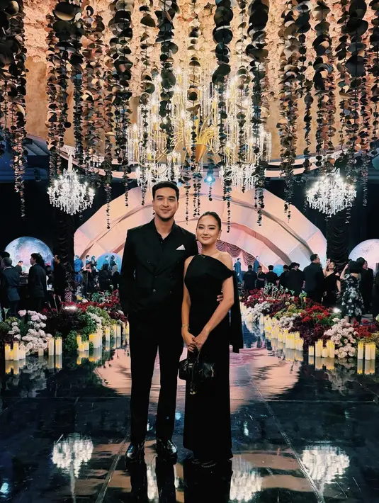 Pasangan Salsa-Ohim tampil serasi dalam balutan busana hitam bernuansa minimalis. Salsa memilih gaun hitam sederhana dengan potongan clean, sementara Ohim mengenakan setelan jas hitam tailored yang rapi. Kesan sleek dan modern sangat terasa, selaras dengan ambience mewah lokasi acara. [@shalsabilladr].