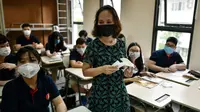 Seorang guru membagikan masker kepada siswa di dalam kelas di sekolah Marie Curie di Hanoi, Senin (4/5/2020). Vietnam membuka kembali aktivitas sekolah yang ditutup selama tiga bulan setelah dilaporkan tidak ada kasus virus corona COVID-19 baru hingga Sabtu, 2 Mei 2020. (Manan VATSYAYANA/AFP)