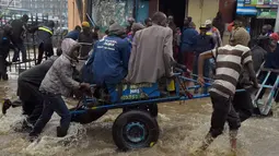 Pejalan kaki menggunakan gerobak melintasi banjir dalam perjalanan ke tempat kerja setelah hujan deras di Nairobi, Kenya (15/3). (AFP Photo/Simon Maina)