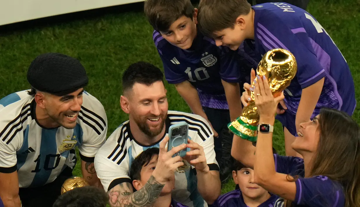 Pemain Argentina Lionel Messi memotret istrinya Antonela Roccuzzo yang memegang trofi Piala Dunia 2022 usai mengalahkan Prancis pada pertandingan sepak bola final Piala Dunia 2022 di Stadion Lusail, Lusail, Qatar, 18 Desember 2022. Argentina menang 4-2 atas Prancis melalui drama adu penalti setelah pertandingan berakhir imbang 3-3. (AP Photo/Francisco Seco)