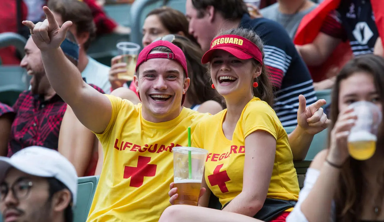Seorang wanita bersama pasangannya tersenyum saat menyaksikan hari pertama turnamen rugby sevens Hong Kong, China (6/4). Turnamen ini diadakan setiap tahun di Hong Kong pada akhir pekan di akhir Maret atau awal April. (AFP Photo/Isaac Lawrence)