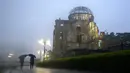 Dua pria berjalan di tengah hujan lebat di dekat Kubah Bom Atom di Hiroshima, Jepang barat,  Kamis (15/7/2021). Gedung ini dibiarkan begitu saja untuk memperlihatkan efek bom atom. Gedung ini berjarak sekitar 160 meter dari pusat ledakan (hypocenter). (AP Photo/Eugene Hoshiko)