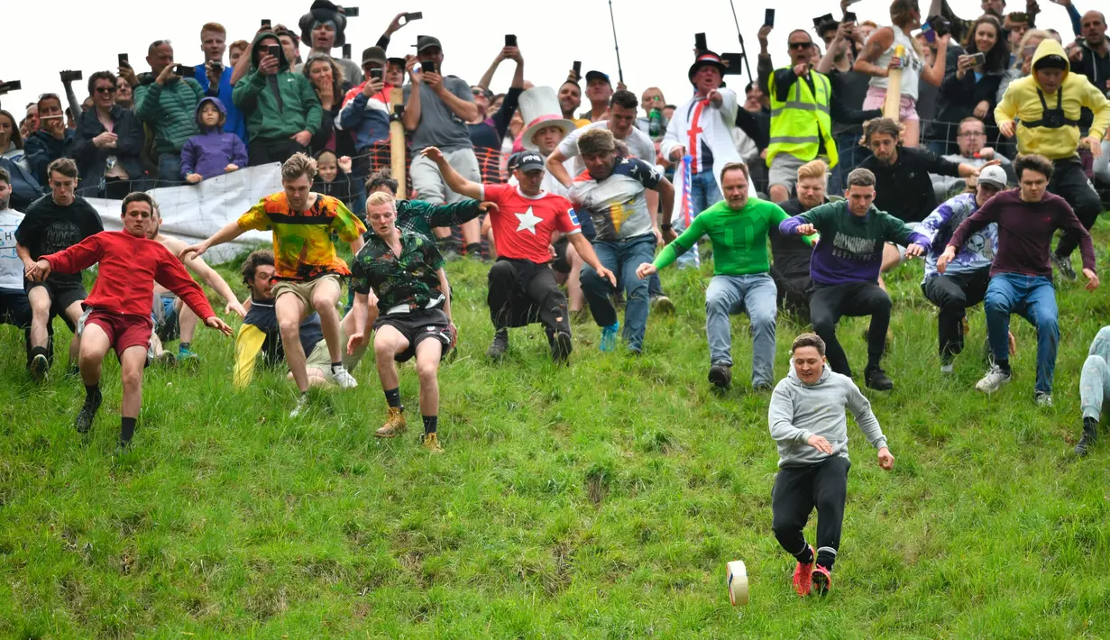 Peserta berlomba mengejar keju dalam kompetisi Cheese Rolling di Bukit Cooper, Gloucestershire, Inggris, Senin (27/5/2019). Acara ini awalnya dibuat oleh dan untuk penduduk lokal namun, kini ribuan orang datang dari berbagai penjuru dunia untuk menonton maupun berpartisipasi (Ben Birchall/PA via AP)