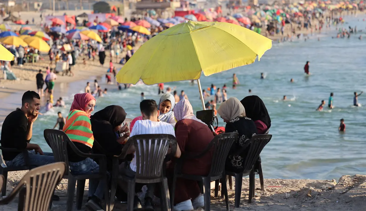 Warga Palestina berkumpul di pantai Beit Lahia di Jalur Gaza utara saat para siswa memulai liburan musim panas mereka pada 3 Juni 2022. Sejumlah warga menikmati musim panas dengan berenang dan bermain air di pantai. (MOHAMMED ABED / AFP)