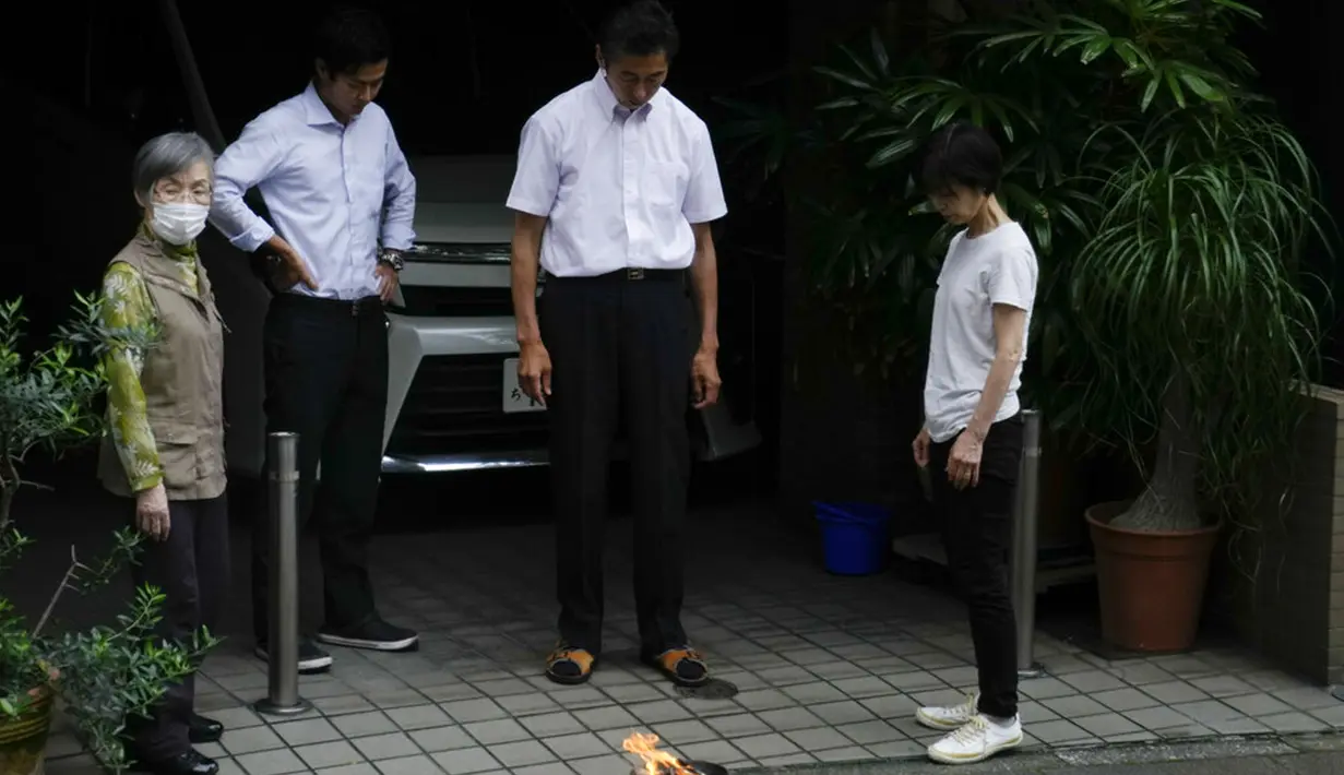Satu keluarga melihat api kecil yang menyala di luar rumah mereka untuk menghormati leluhur di Tokyo, Jepang, Selasa (13/7/2021). Keadaan darurat akan berlaku sepanjang Olimpiade yang dibuka pada 23 Juli. (AP Photo/Jae C. Hong)