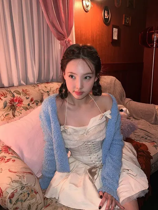 Nayeon Twice juga kerap tampil dengan gaya Coquette yang manis. Pada potret ini, ia memadukan corset dress dengan aksen pita dan wool cardigan warna biru pastel. [@nayeonyny]