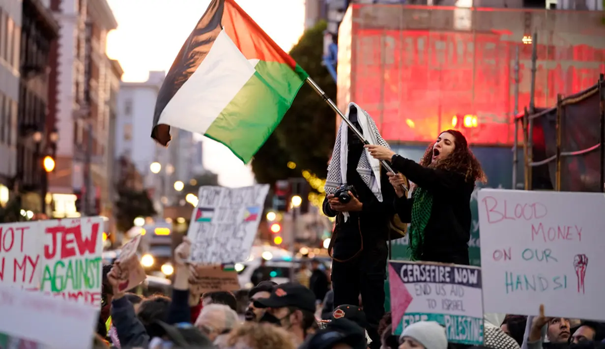 Seorang pengunjuk rasa mengibarkan bendera Palestina saat melakukan protes menentang perang Israel-Hamas bersamaan dengan KTT APEC yang berlangsung di San Francisco, Amerika Serikat, Selasa (14/11/2023). (AP Photo/Godofredo A. Vásquez)