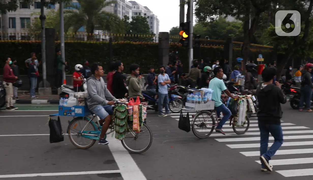 Pedangang menawarkan dagangannya kepada massa aksi saat demo penolakan omnibus law di kawasan patung kuda, Jakarta, Selasa (20/10/2020). Para pedagang kaki lima memanfaatkan moment aksi massa untuk mencari ke untungan meskupun sangat membahayakan bagi keselamatan mereka. (Liputan6.com/Angga Yuniar)