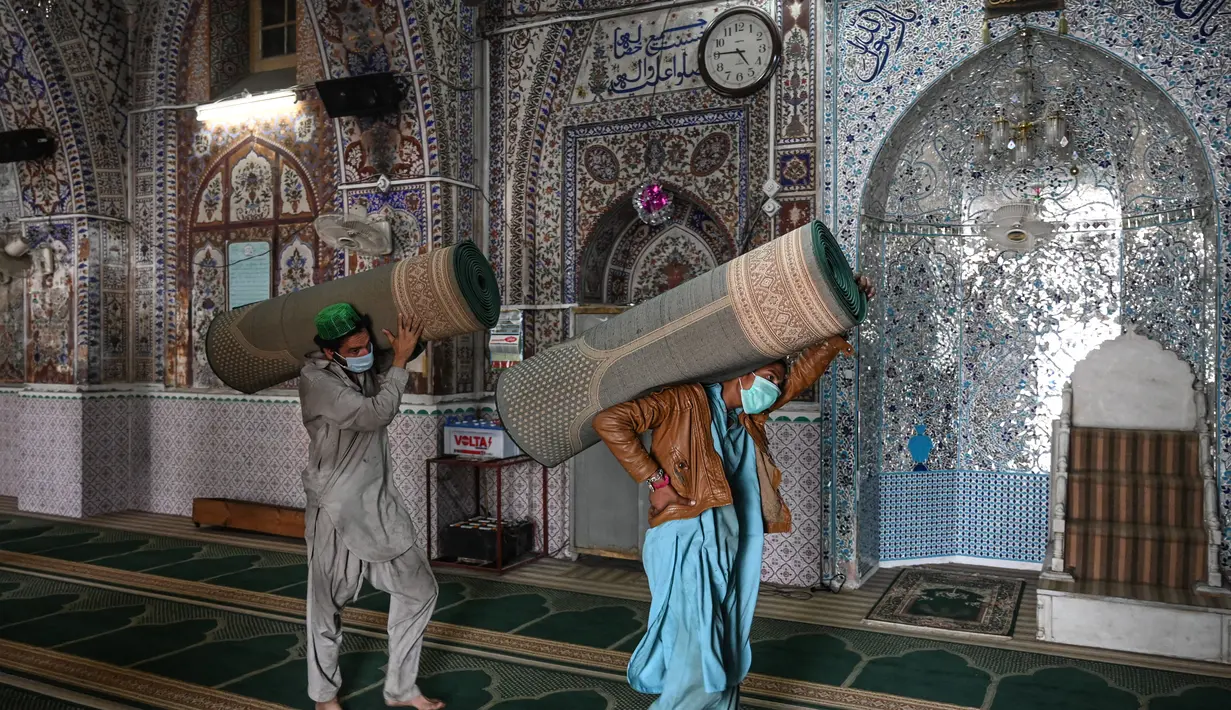 Umat Muslim membawa karpet sajadah dari aula utama masjid menyusul pembatasan baru pemerintah baru menjelang bulan suci Ramadan di Rawalpindi, Pakistan, Senin (5/4/2021). Sesuai pedoman, barisan orang yang salat harus sejajar sehingga ada jarak enam kaki antarindividu. (Aamir QURESHI/AFP)