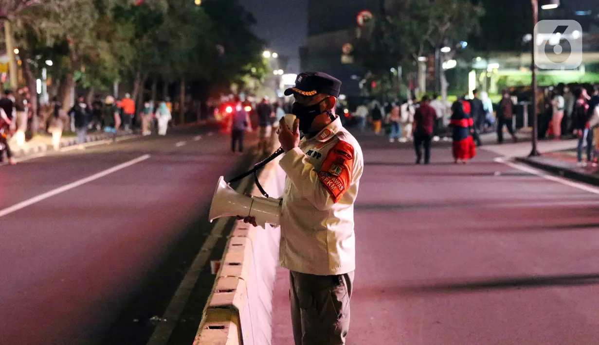 Satpol PP melakukan imbauan menggunakan pengeras suara terhadap warga yang berkerumun di kawasan Bundaran HI, Jakarta, Jumat (31/12/2021). Petugas gabungan melarang perayan malam pergantian tahun di wilayah Jakarta untuk mencegah penyebaran COVID-19. (Liputan6.com/Angga Yuniar)