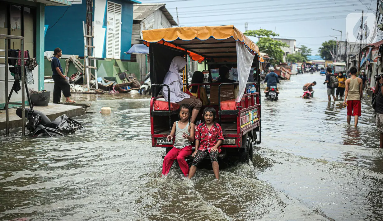 Anak-anak duduk di belakang kendaraan yang melintas saat banjir rob di Muara Angke, Jakarta, Jumat (25/11/2022). Badan Penanggulangan Bencana Daerah (BPBD) DKI Jakarta mengimbau agar warga di pesisir Jakarta mengantisipasi banjir pesisir atau rob selama 22-28 November 2022. (Liputan6.com/Faizal Fanani)