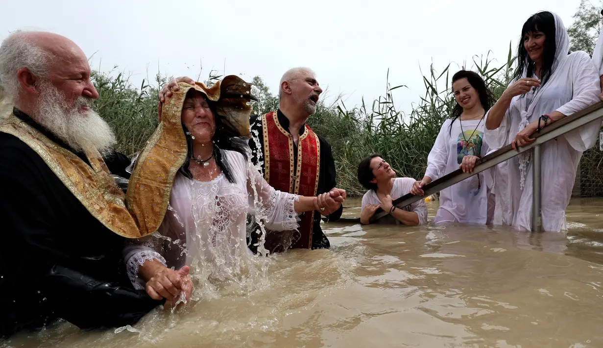 Imam Kristen Ortodoks Serbia membaptis wanita di perairan Sungai Yordan di dekat kota Jericho (4/3). Sungai ini diyakini menjadi tempat Yesus Kristus dibaptis oleh Yohanes Pembaptis.  (AFP Photo/Gali Tibbon)