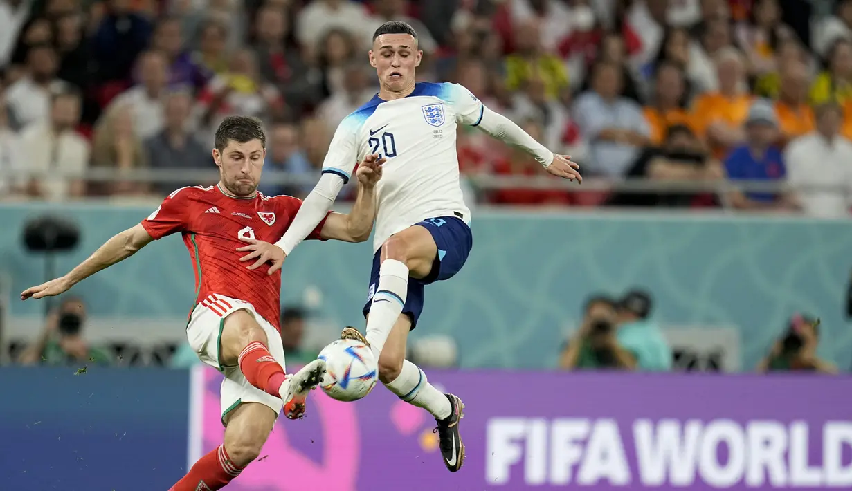Bek Wales Ben Davies berebut bola dengan gelandang Inggris Phil Foden pada pertandingan terakhir Grup B di Ahmad bin Ali Stadium, Rabu (30/11/2022) dini hari WIB.Inggris mencetak seluruh golnya di babak kedua lewat sepasang gol Marcus Rashford yang dilengkapi Phil Foden. (AP Photo/Abbie Parr)