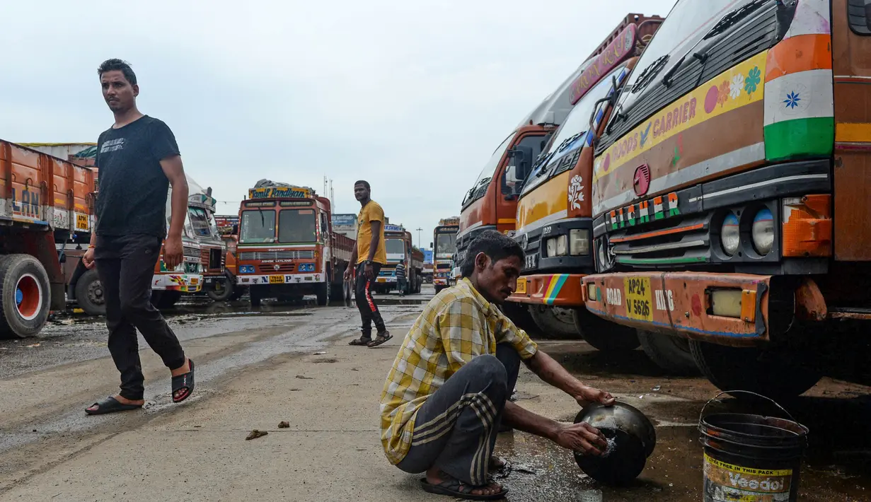 Seorang sopir mencuci di samping sebuah truk yang diparkir di sebuah terminal di Chennai (19/9/2019). Akibat pemogokan layanan transportasi, beberapa sekolah di ibukota nasional akan diliburkan saat pemogokan satu hari tersebut. (AFP Photo/Arun Sankar)