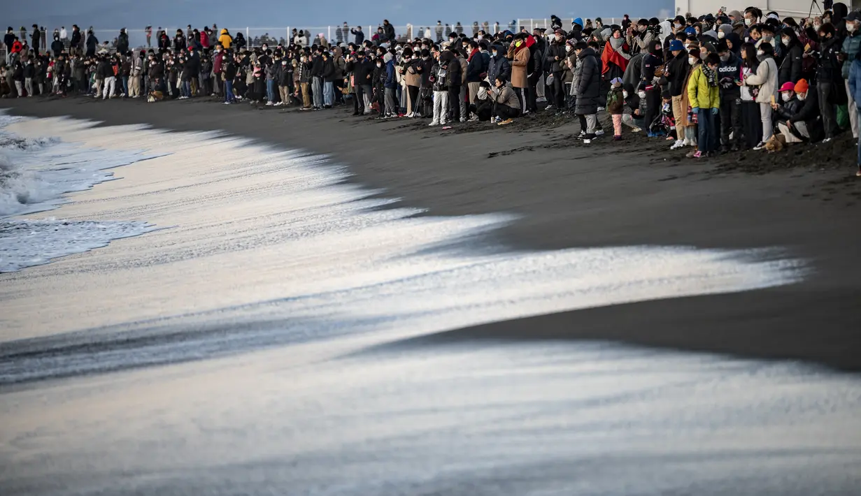 Orang-orang berkumpul di Pantai Selatan Chigasaki untuk menyaksikan matahari terbit pada Hari Tahun Baru di Prefektur Kanagawa, barat daya Tokyo (1/1/2021). (AFP/Philip Fong)