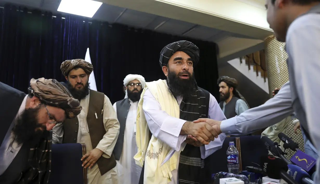 Juru bicara Taliban Zabihullah Mujahid, berjabat tangan dengan seorang wartawan setelah konferensi pers pertamanya, di Kabul, Afghanistan, pada Selasa (17/8/2021). Selama bertahun-tahun, Mujahid adalah sosok misterius yang mengeluarkan pernyataan atas nama para militan. (AP Photo/Rahmat Gul)