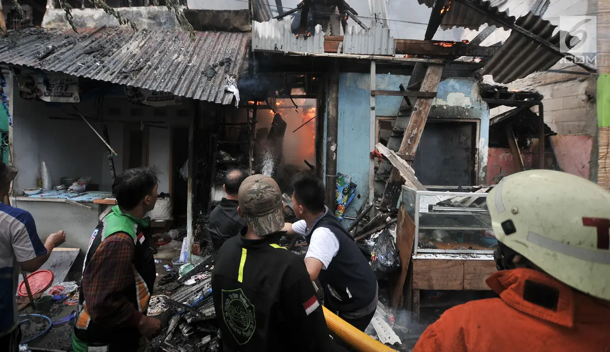 Warga menjinakkan kobaran api yang membakar permukiman di kawasan Tanah Tinggi, Johar Baru, Jakarta, Selasa (26/6). Sejumlah warga memilih mengungsi ke pinggir rel yang berada tidak jauh dari lokasi kebakaran. (Merdeka.com/Iqbal Nugroho)